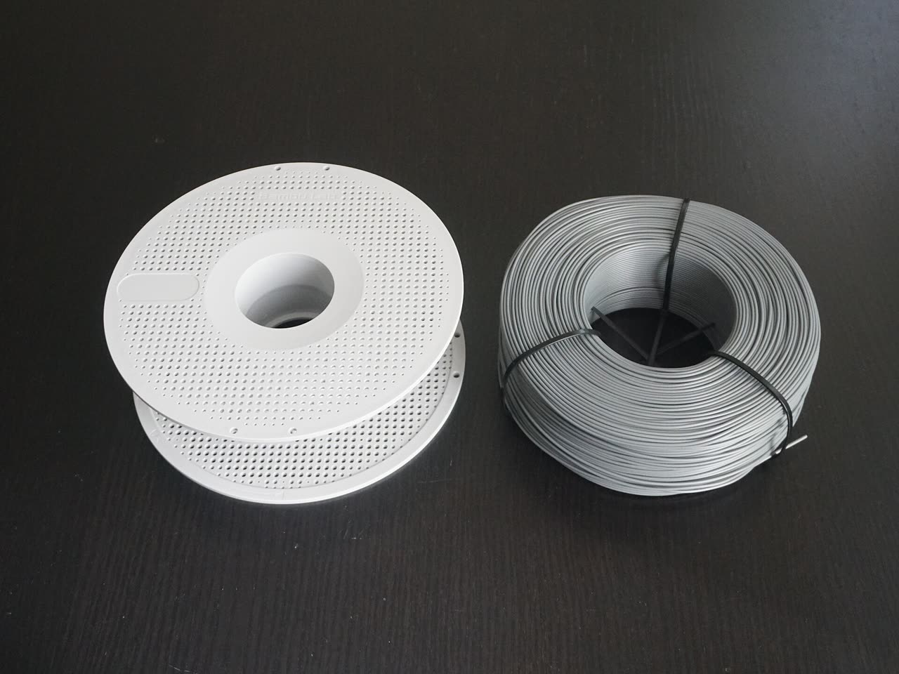 An empty white Bambu Lab spool next to a grey filament refill held together with black zip ties.